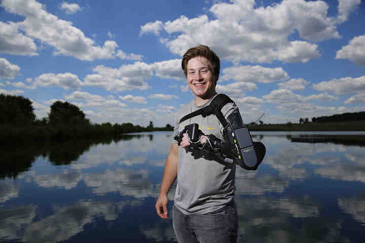 18-year-old Zeke Dees of Mechanicsburg stands beside his family pond wearing his myomo MyoPro brace. Dees suffered an arm injury on an ATV when he was 8-years-old and lost much of the ability to use his left arm until he got the MyoPro nearly a year ago.  (Adam Cairns / The Columbus Dispatch)